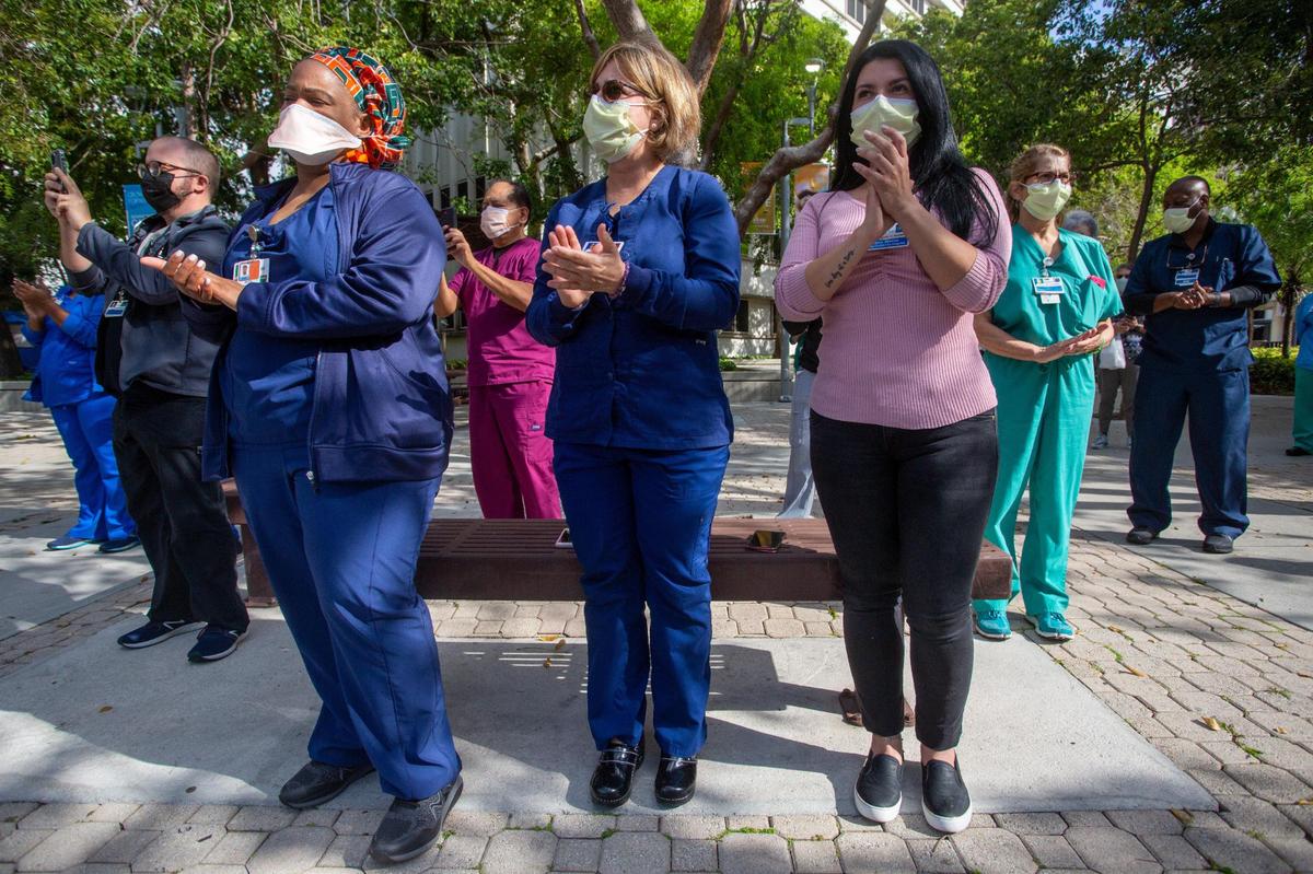 Nurse practitioner Ruth Dassas-Molin, left, pediatric nurse Aymee Morales Aranegui, center, and pediatric coordinator Francis Jimenez attend a ceremony honoring healthcare workers and patients affected by the COVID-19 pandemic, with an installment of 5,200 blue flags representing the lives saved and 1,000 white flags honoring the lives lost on the first anniversary of the pandemic. The ceremony was held at Jackson Memorial Hospital in Miami, Florida, on Friday, March 19, 2021.