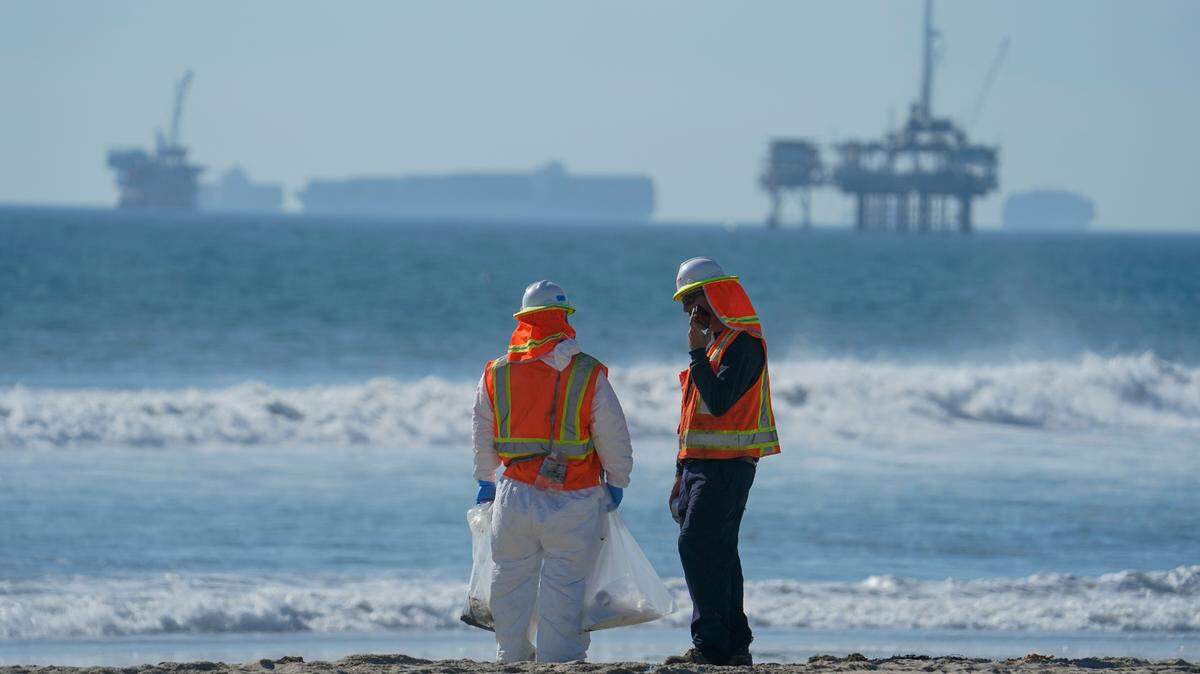 In 2021, members of a cleanup crew stand along Huntington Beach, California. More than 125,000 gallons of oil spilled from a pipeline four miles off Southern California’s coast.