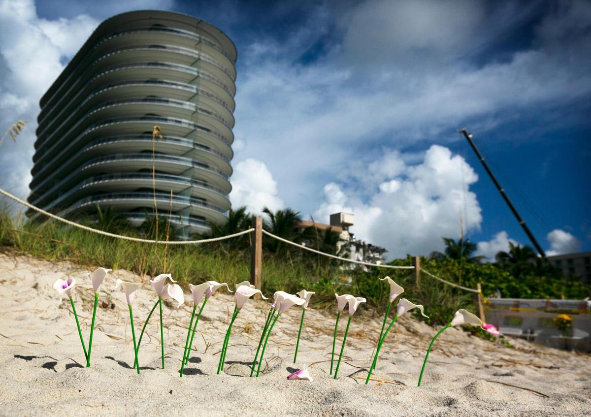 Plastic flowers are planted in the sand as a memorial south of where workers continue their search at the collapsed Champlain Towers South site Friday morning, July 2, 2021, on Day 9 of search-and-rescue efforts.