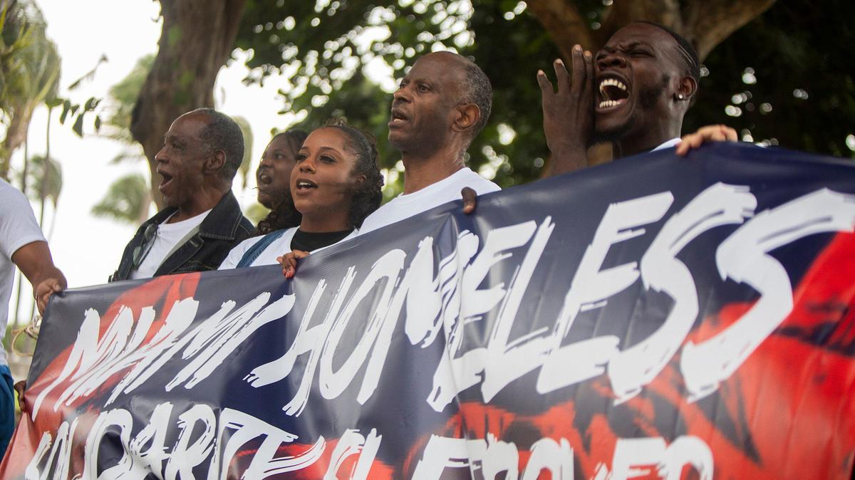 Protesters hold up a sign during a protest about the arrests of homeless people at Lummus Park in Miami Beach on Saturday, Aug. 3, 2024.