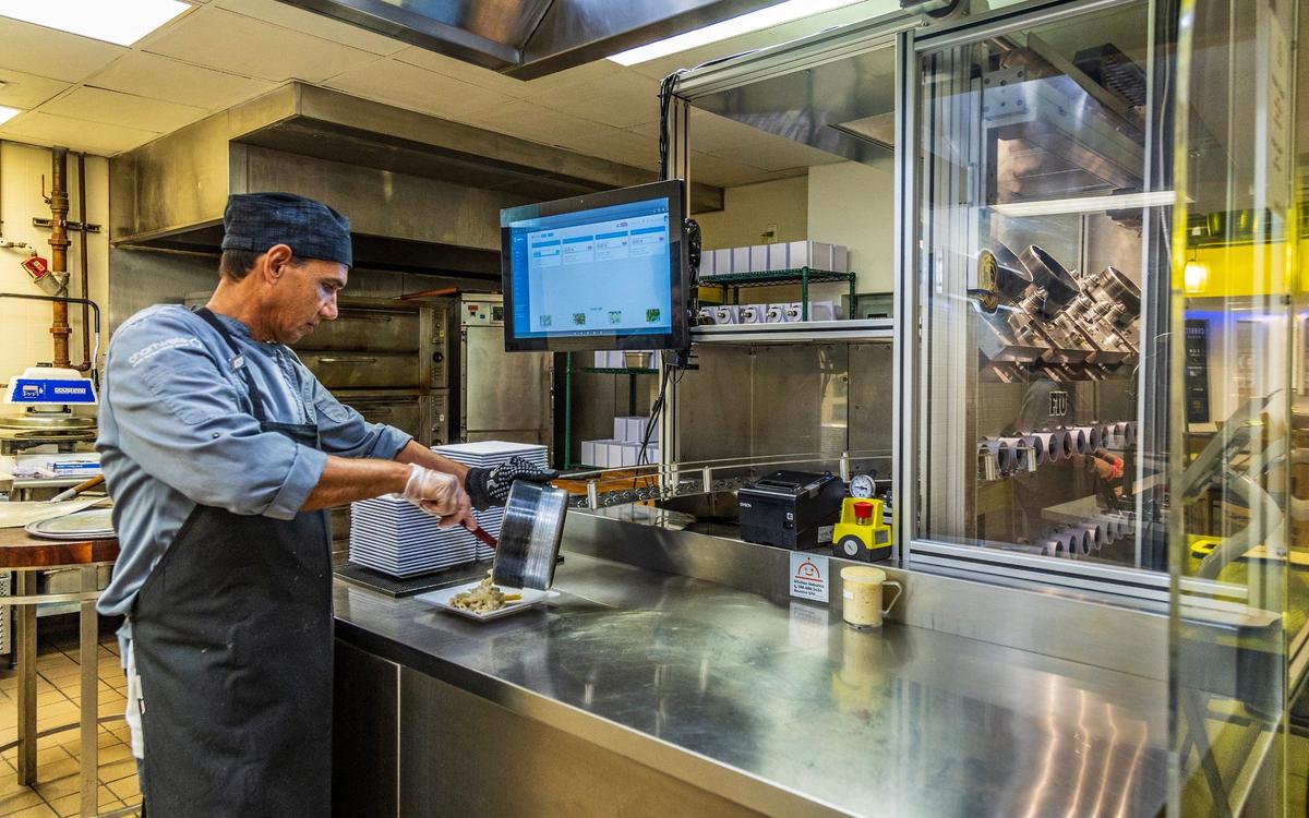 Kitchen assistant Samuel Hurtado plates a serving of pasta after it has been cooked by Beastro, the self-contained robotic kitchen at FIU.