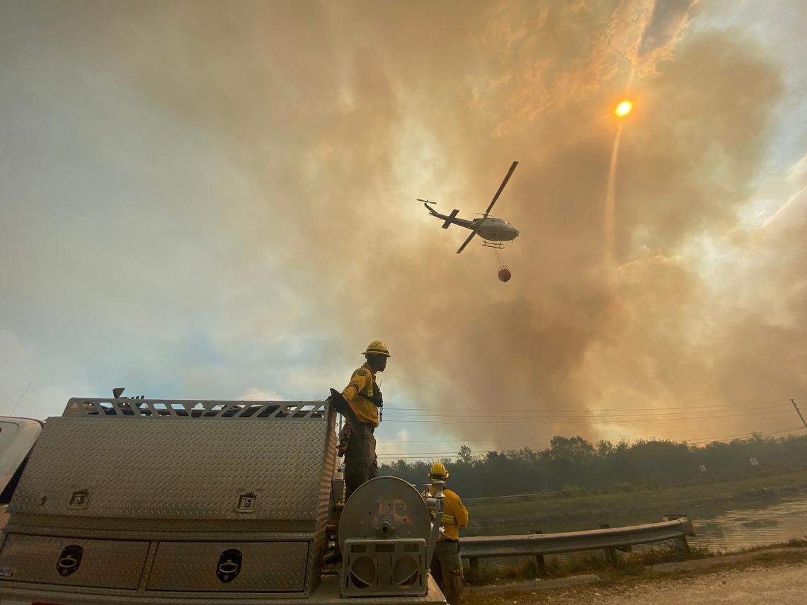 A helicopter drops water over the fire at Southwest 344th Street and 117th Avenue in Homestead on Thursday afternoon, March 20, 2025. The brush fire had started around Card Sound Road near Florida City but by Thursday, the fire had spread to Homestead. Authorities said the fire was burning 22,000 acres of brush — with 22% containment.