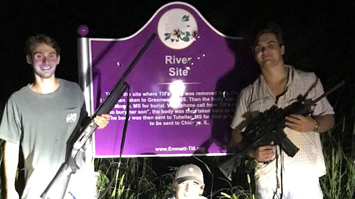 Three white University of Mississippi students, two holding weapons, posed in front of a sign marking where the body of Emmett Till, an African-American teenager was recovered from the Tallahatchie River in 1955.