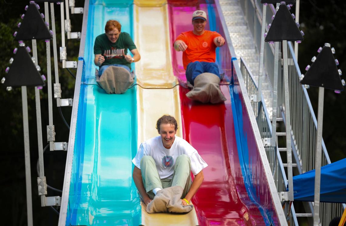 Chris Rhoades, senior, center, Camden Slinger, senior, left, and Paul Rhoades, alumni, ride down the slide during the University of Miami Centennial celebration on Tuesday, April 8, 2025, on Foote University Green at the University of Miami’s Coral Gables campus.