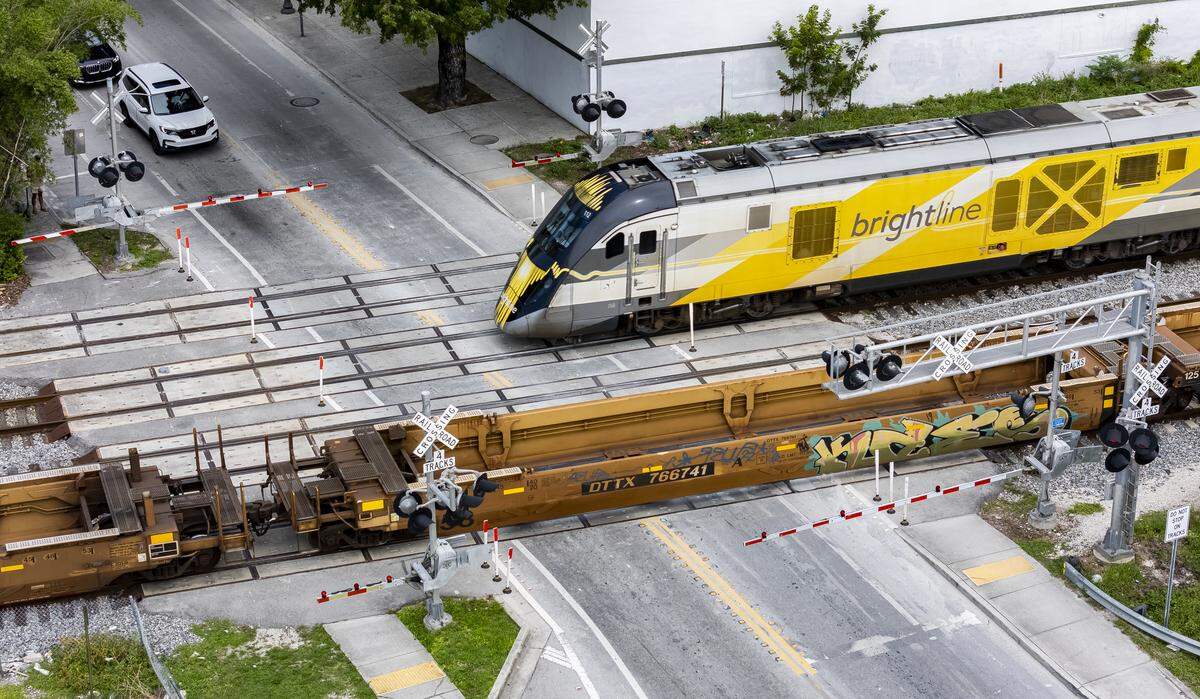 A Florida East Coast Railway (FEC) freight train and a Brightline train run on parallel tracks through Miami at Northwest 14th Street near First Avenue. The dual trains have confused some drivers who don’t see the second train coming.