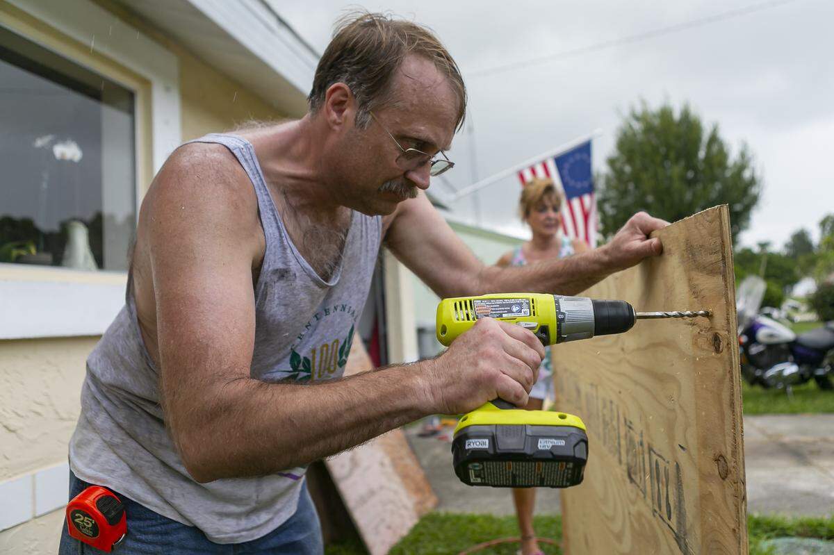 Colin Johnson, 51, drills plywood as he prepares to board up a window of his father’s home.