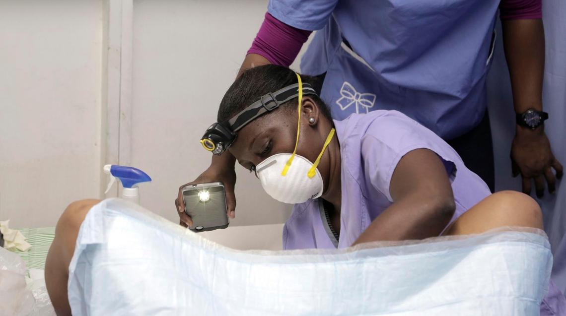 An assistant uses a cellphone light to guide Nanotte Louis, a midwife with Innovating Health International, as she prepares to treat a precancerous lesion on a woman’s cervix, at the Caribbean Island Apparel factory in Port-au-Prince.