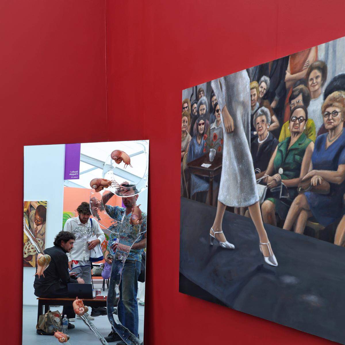Miami Beach, FL, December 2, 2025 -  Two artists share exhibition space as Untitled Art fair attendees take moment to catch their breaths as their reflection is casted Sam Shawzin's artwork “Pissing Contest”, left, displayed next to the artwork of Ray DellaMura during the fair's opening day 