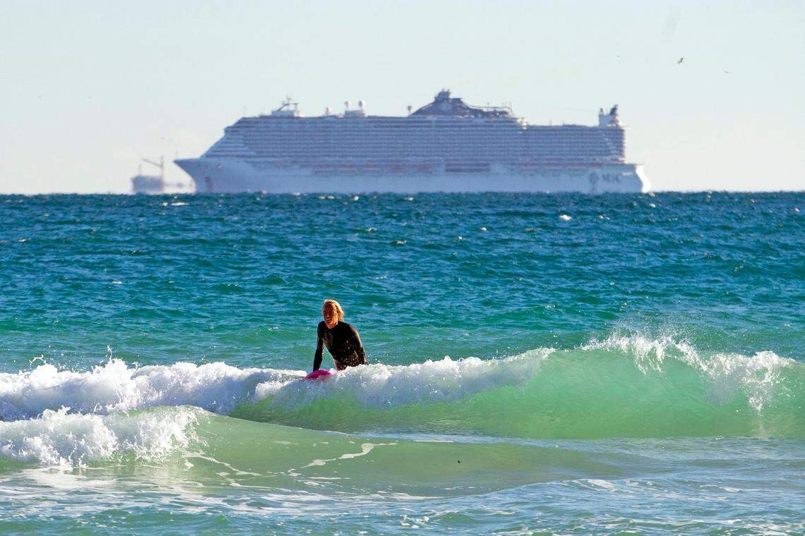 A cruise ship is seen out at sea as a surfer tries to catch waves under cold weather at South Pointe Beach on Wednesday, Dec. 9, 2020, in Miami Beach, Florida.