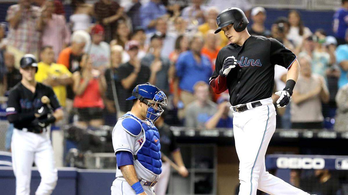 Miami Marlins Garrett Cooper (26) runs past New York Mets catcher Wilson Ramos (40) to score after Cooper hit the Marlins second home run in the third inning at Marlins Park in Miami, Florida, Friday, July, 12, 2019.