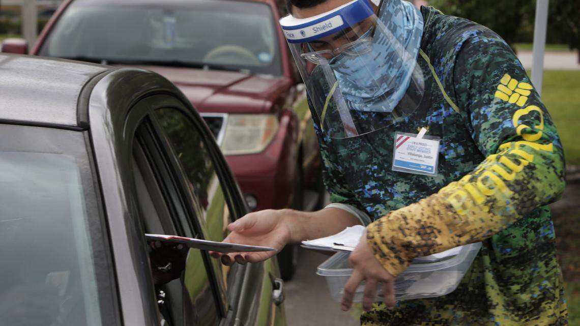 Poll worker Justin Villalonga accepts a mail-in ballot from a voter at the North Dade Regional library in Miami Gardens during the first day of early voting, Oct. 19, 2020. Many voters drove and walked to the site to deposit ballots in drop boxes behind the library.