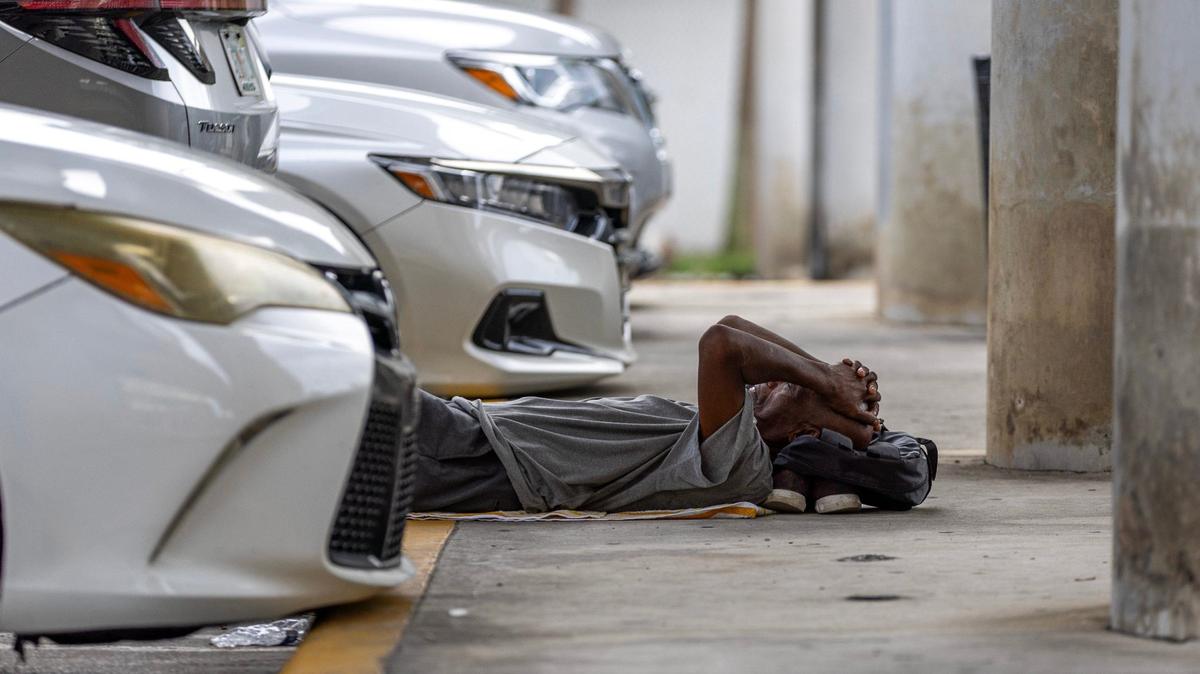 A man sleeps inside a parking lot underneath the expressway while waiting for the nonprofit One World One Heart to deliver free meals to the homeless population on Thursday, Sept. 12, 2024, in Miami.