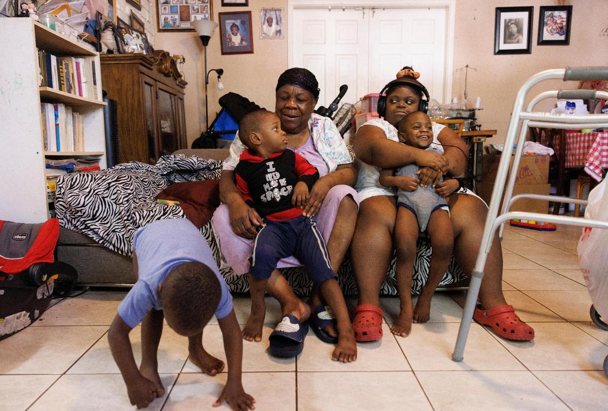 Mimose Martial, center, sits on the couch with Yahwe, 3, while Yeshousa, 2, left, plays and his twin, Samson, 2, right, sits on the lap of Marie, Mimose’s daughter, right, inside their Miami home.