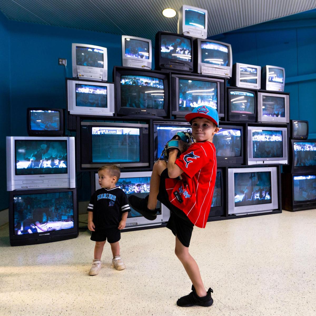 Riley Christiansen, de siete años, mostrando su mejor postura de lanzamiento mientras su hermano menor Colton, de dos años, mira mientras recorre Miami Marlins 30th Anniversary History Museum dentro de LoanDepot Park el miércoles 17 de mayo de 2023.