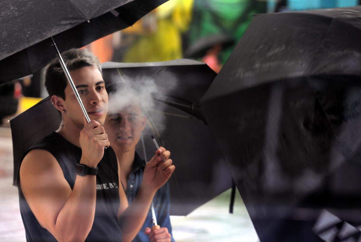 Group of men huddle underneath umbrellas as rain comes down in Wynwood Art District on Sunday, June 16, 2019. Miami Herald file