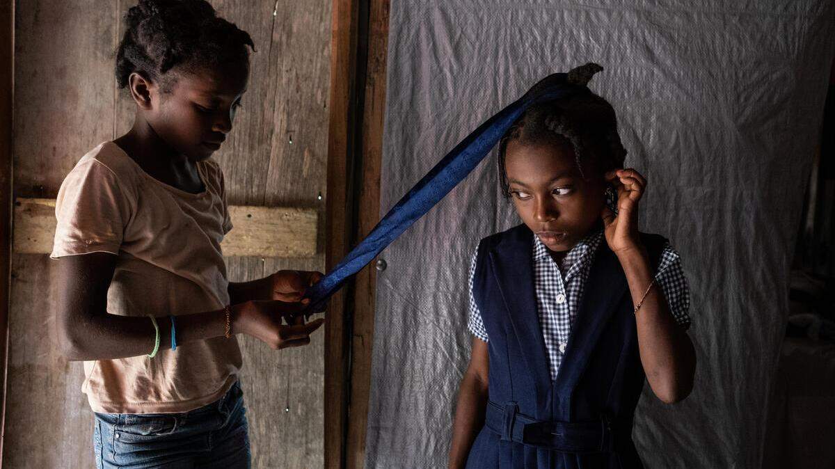 Entha, 10, at right in school uniform, has her hair braided by a friend in her home in southwest Haiti. Her village was destroyed during the earthquake, and her mother, Edlène, received three cash transfers from Save the Children to help rebuild the house, feed the children and pay scholarships so they could go to school.
