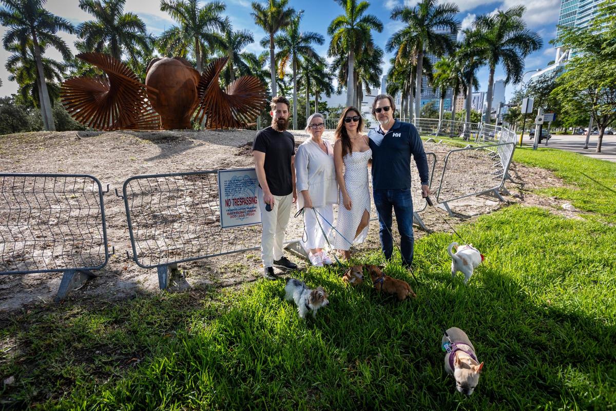 Miami, Florida, Oct. 6, 2023 - Left to right, Max Mendez and his dog Domino, Candace O’Brien with her dogs Iris and Ruth, Kelly Sabo with Gigi and TJ Sabo with Stella at the site where one of the oldest trees in Maurice Ferré Park in downtown Miami once stood. The city chopped down the 35-foot tall ficus tree, saying people were tripping over its roots. The neighbors dispute that and are irate over the tree’s removal. Now, there’s a sculpture on the site