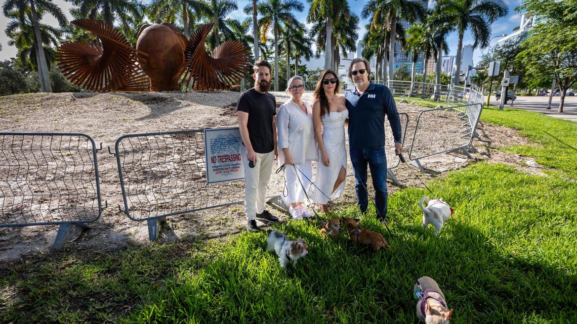 Miami, Florida, Oct. 6, 2023 - Left to right, Max Mendez and his dog Domino, Candace O’Brien with her dogs Iris and Ruth, Kelly Sabo with Gigi and TJ Sabo with Stella at the site where one of the oldest trees in Maurice Ferré Park in downtown Miami once stood. The city chopped down the 35-foot tall ficus tree, saying people were tripping over its roots. The neighbors are irate over the tree’s removal. A Miami planning board ruled Wednesday, Nov.15, 2023, that the city has to remove an outdoor gym at the park.