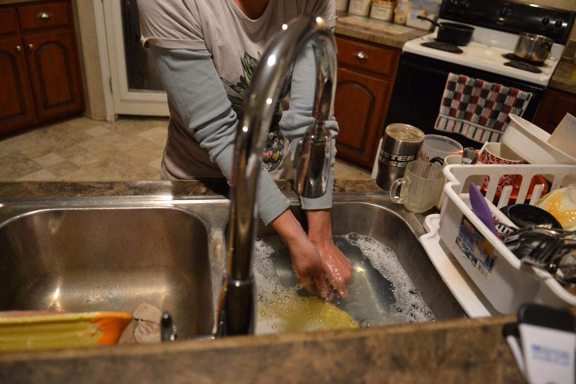 Linda Lawson’s daughter-in-law, Jessica, washes dishes in the family home. Though someone from the health department brings the family 5-gallon jugs of water for consumption purposes, the family continues to use well water for showering and washing dishes.