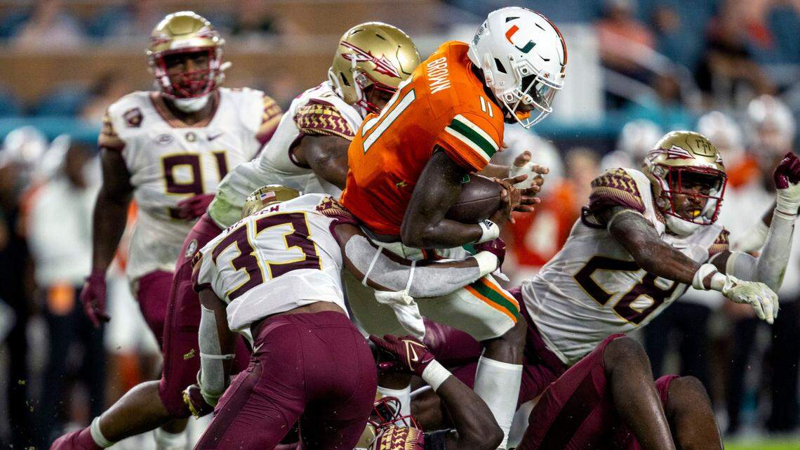 Miami Hurricanes quarterback Jacurri Brown (11) is tackled by multiple Florida State University defenders during the second half of an ACC football game at Hard Rock Stadium in Miami Gardens on Saturday, November 5, 2022.