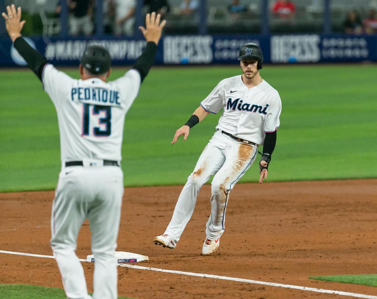 Miami Marlins major league third base coach Al Pedrique (13) signals to third baseman Brian Anderson (15) as he arrives to third base after center fielder Bryan De La Cruz (14) doubles on a ground ball against the Washington Nationals during the second inning of their baseball game at LoanDepot Park on Monday, May 16, 2022, in Miami, Florida.