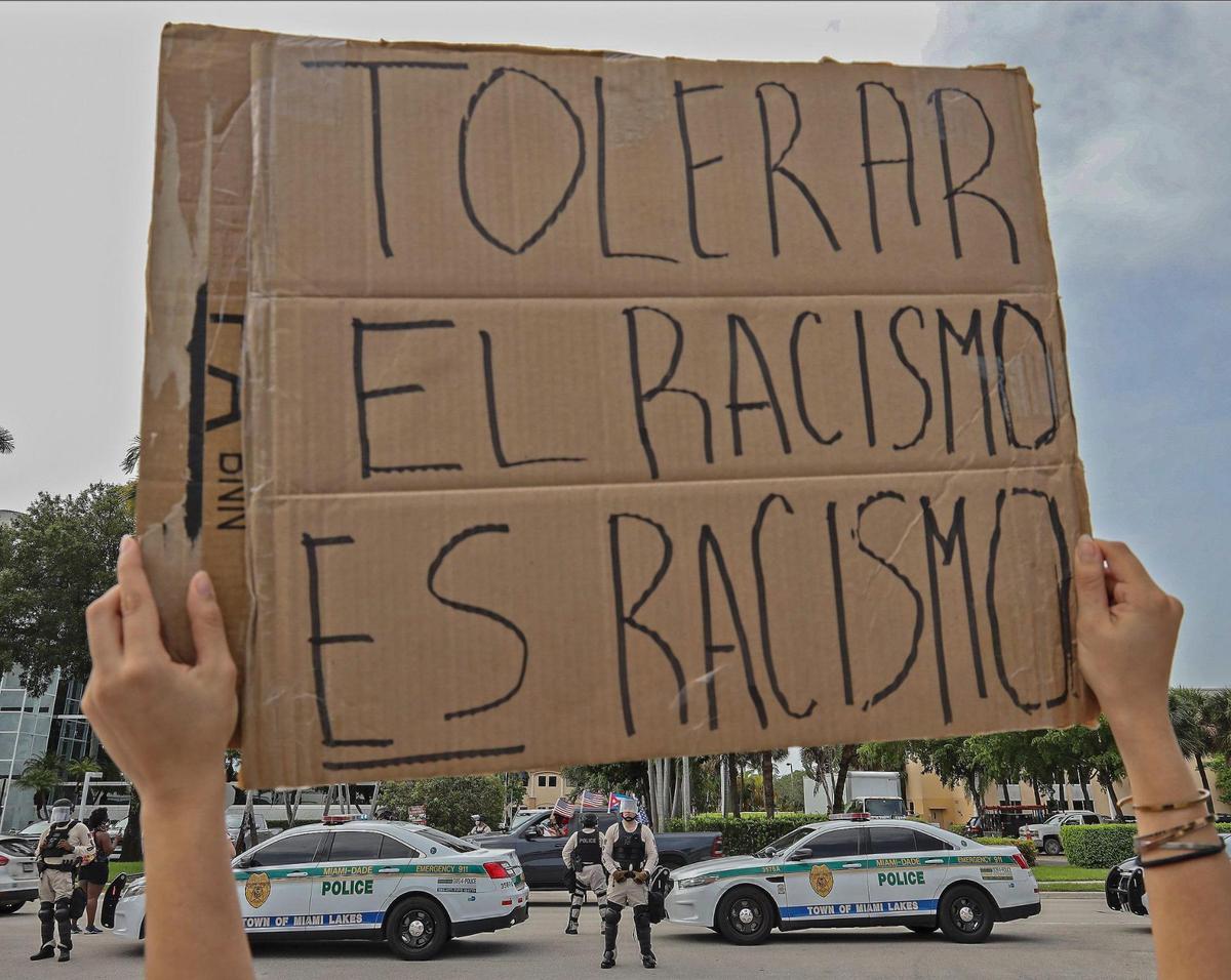 A Black Lives Matter protester holds her sign as Trump supporters and a Black Lives Matter group intersect at a distance at the 7900 block of NW 154th Street in Miami Lakes, Florida, on Sunday, June 28, 2020.