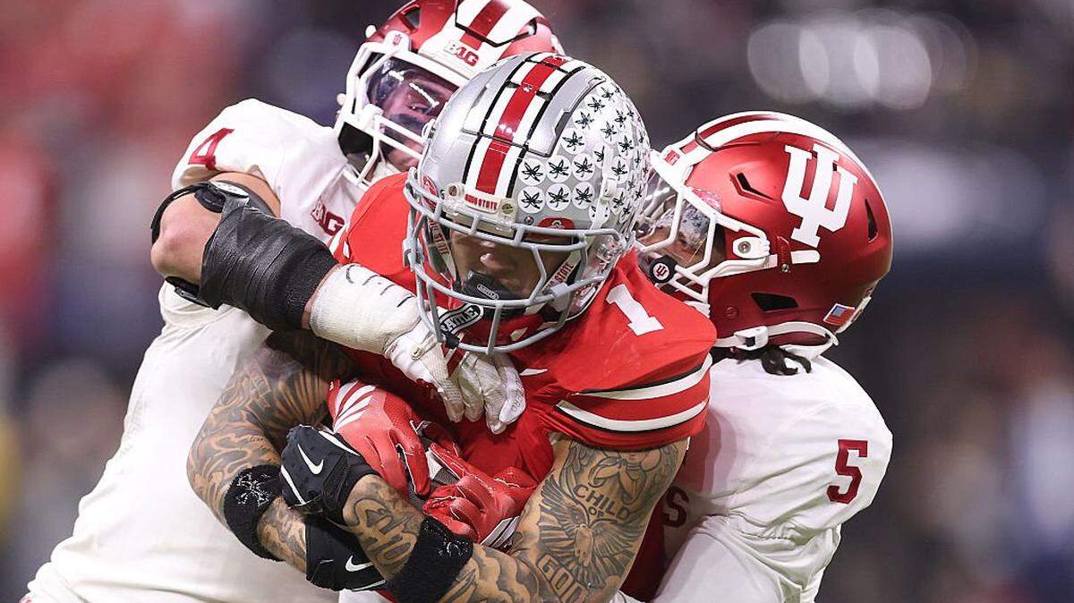 INDIANAPOLIS, INDIANA - DECEMBER 06: Brandon Inniss #1 of the Ohio State Buckeyes is tackled by Aiden Fisher #4 and D'Angelo Ponds #5 of the Indiana Hoosiers in the 2025 Big Ten Football Championship at Lucas Oil Stadium on December 06, 2025 in Indianapolis, Indiana.  (Photo by Michael Reaves/Getty Images)
