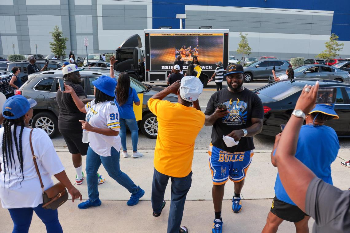 Broadway Harewood, center, and Derrick Madry, right, react as a mobile billboard drives by showcasing highlights of suspended Miami Northwestern football coach and former Miami Dolphins quarterback Teddy Bridgewater during a rally supporting his reinstatement outside of Miami Northwestern Senior High School in Miami, Florida, Thursday, July 24, 2025.