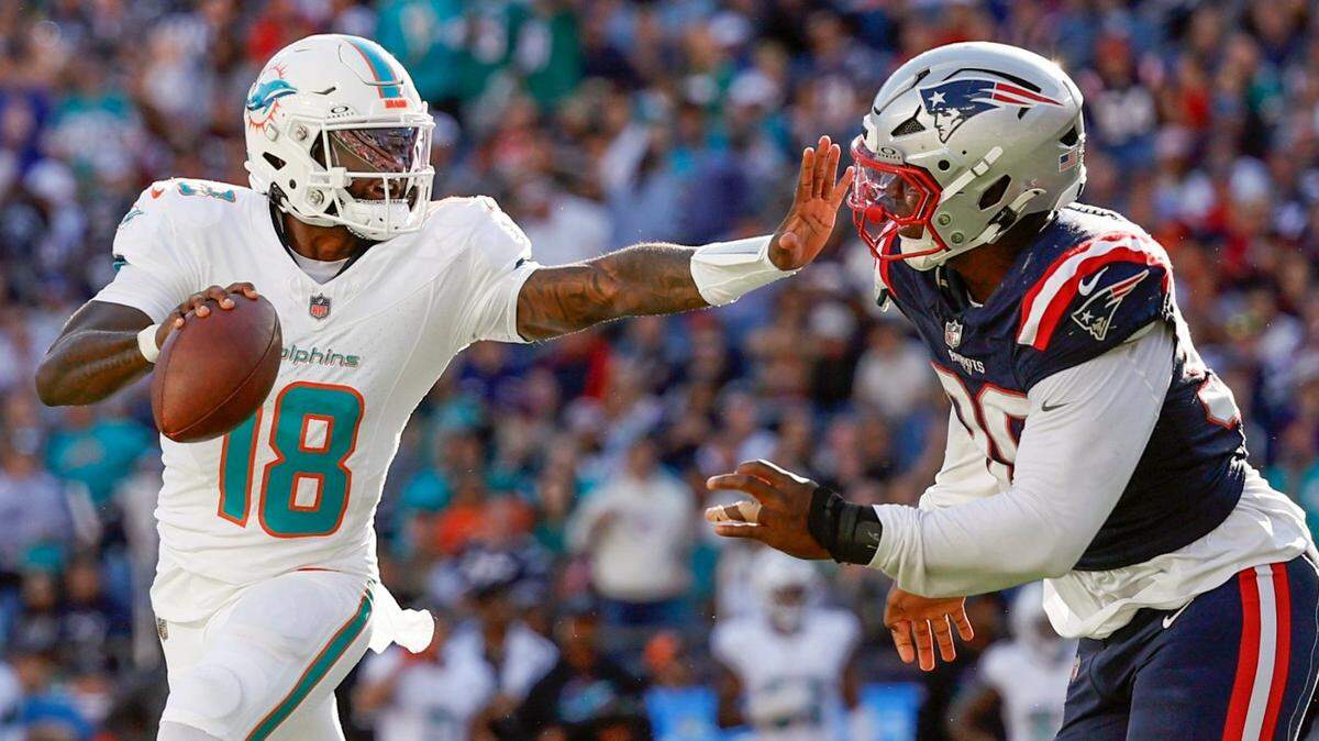 El quarterback de los Dolphins, Tyler Huntley (izq.), intenta pasar el ovoide ante el jugador de los Patriots, Keion White, en la segunda mitad del partido de  la NFL celebrado en el Gillette Stadium en Foxborough, el 6 de octubre de 2024.