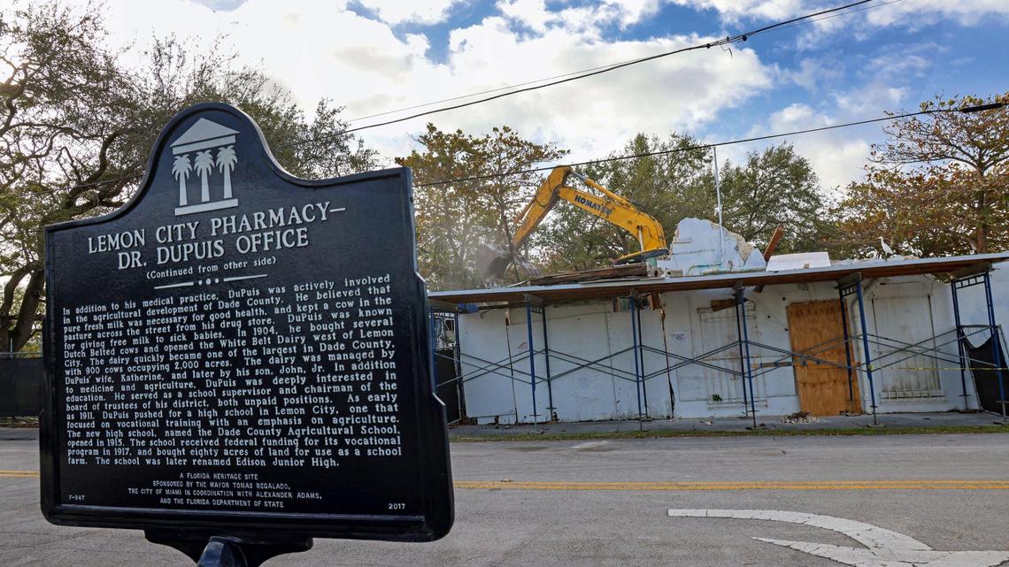 A backhoe takes down the historic, long-vacant DuPuis Medical Office and Lemon City Drugstore, which partially collapsed on January 8, behind its historic marker on Jan. 23, 2024 in Miami’s Little Haiti neighborhood.