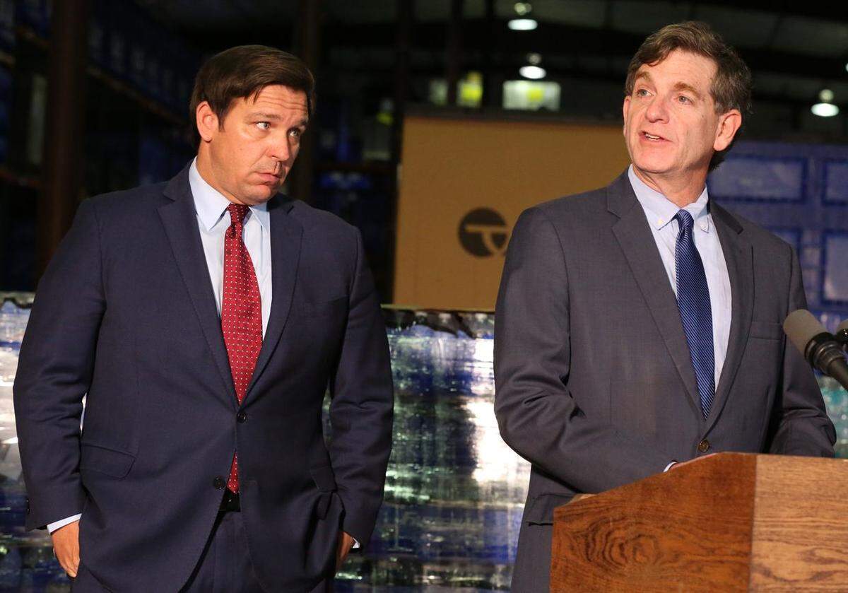 Florida Gov. Ron DeSantis, left listens to Florida Surgeon General Scott Rivkees, right, during a press conference at a Florida Emergency Management warehouse in Tallahassee.