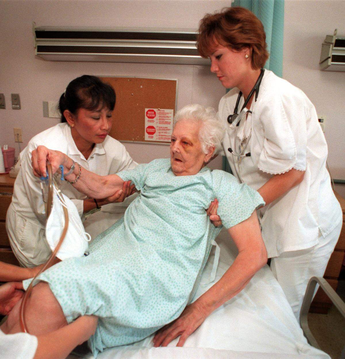 Caridad Baez is helped into her bed in the hospital’s telemetry unit.