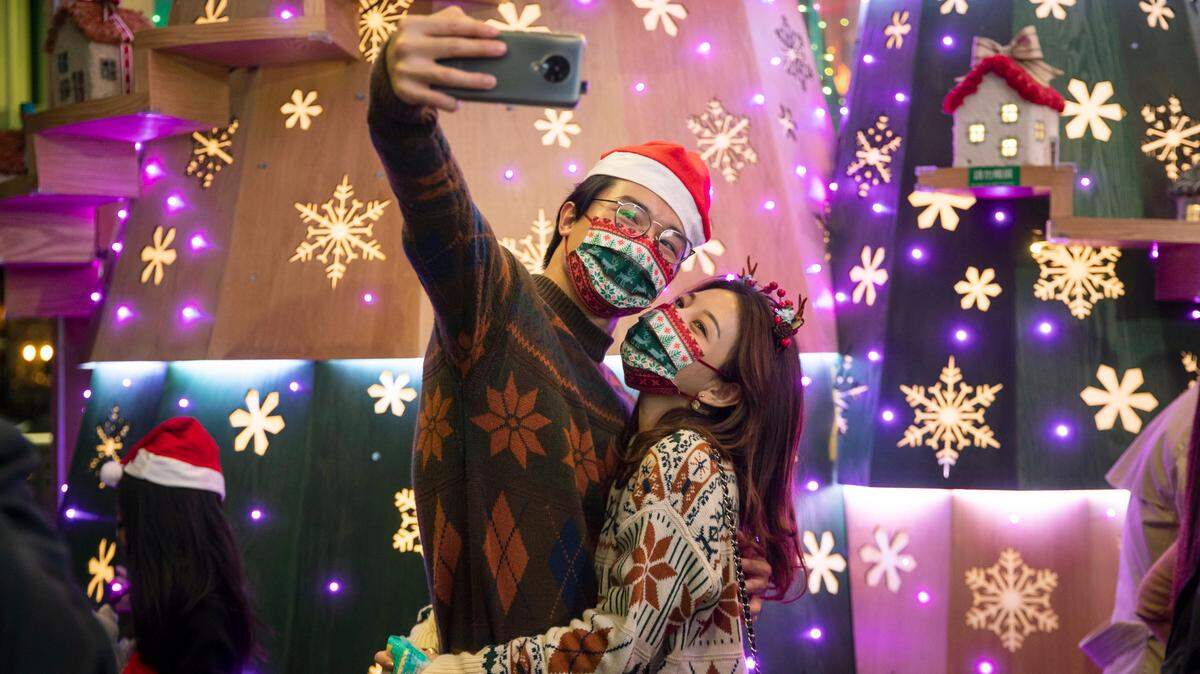 A couple wearing protective masks to prevent the spread of coronavirus, take a selfie in front of Christmas decorations in Hong Kong, Thursday, Dec. 24, 2020.
