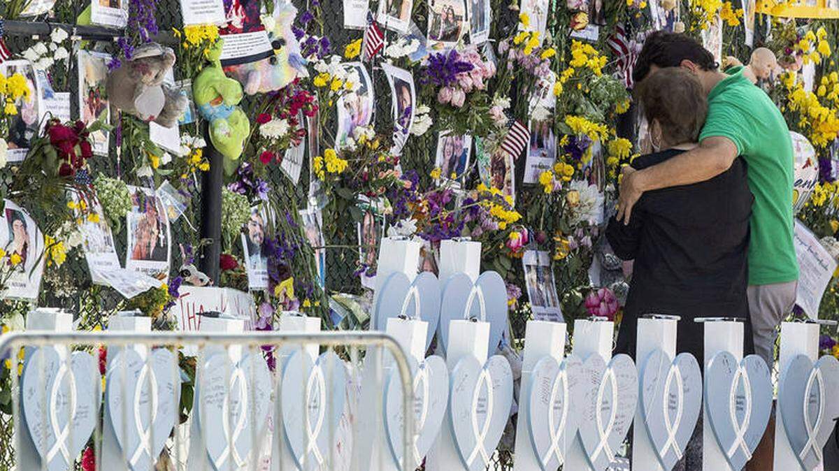 People stand at the memorial wall at the site of the deadly condo collapse in Surfside.