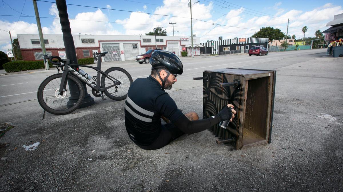 Ahol Sniffs Glue, alias David Anasagasti, un conocido artista local de Miami, se detiene mientras recorre en bicicleta el Pequeño Haití el miércoles 24 de noviembre de 2021, para crear obras de arte con un mueble desechado. Algunas de las piezas que cree a lo largo de su viaje se usarán en su proyecto llamado "Geographies of Trash; Art Cycling with Ahol Sniffs Glue".