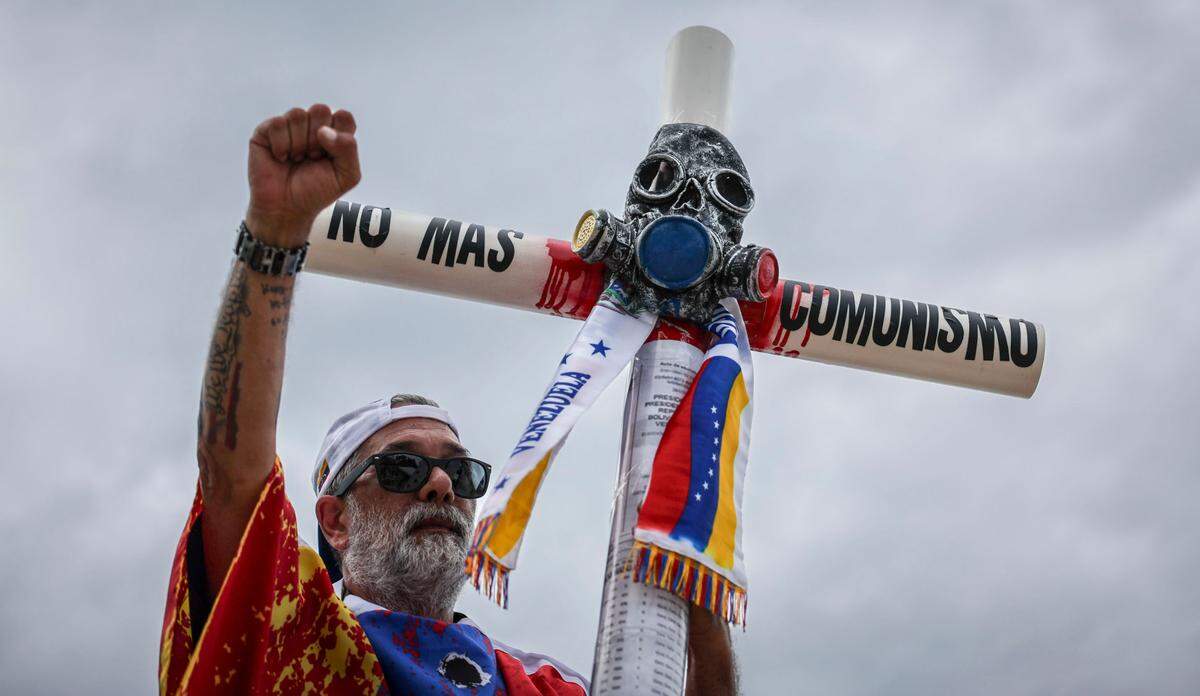 Carrying a cross that bears the words ‘No More Communism’ Gaston Gonzalez arrives at the rally at Bayfront Park in downtown Miami, Fla.