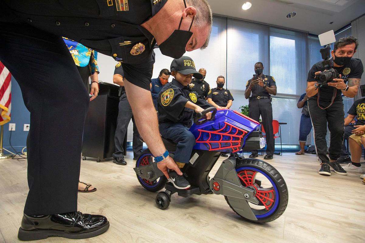 Jeremiah Valera gets a new motorcycle at the North Miami police department on March 20, 2021. Police Chief Larry Juriga helps him adjust his foot.
