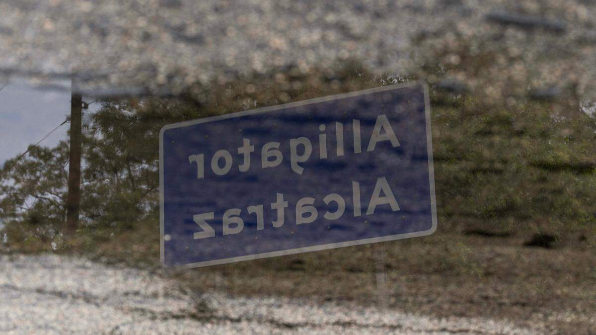 Signage for Alligator Alcatraz is seen in the reflection of a puddle outside the entrance to the center on Sunday, July 13, 2025, in Ochopee, Fla.