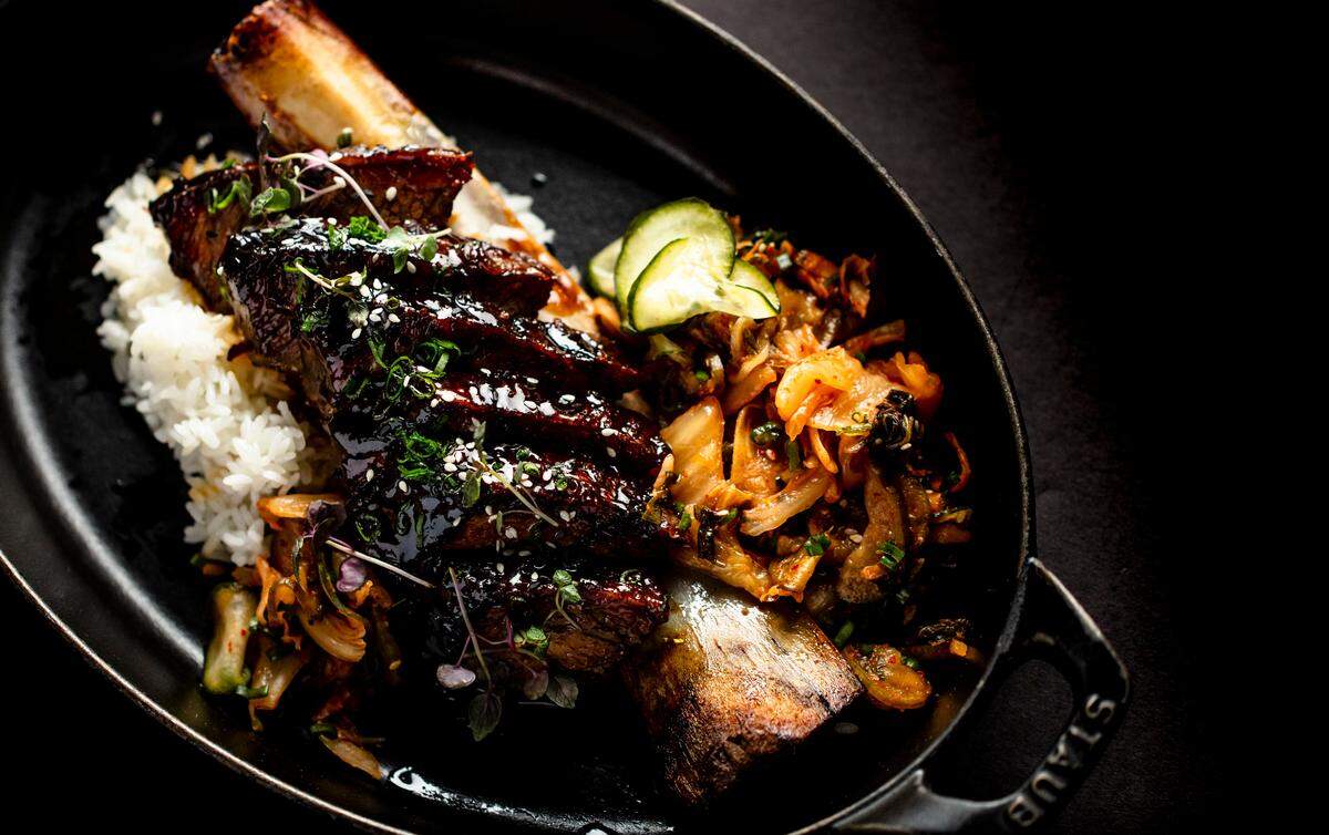 Korean short rib is served on the bone in a cast iron pot accompanied by kimchi and sticky rice