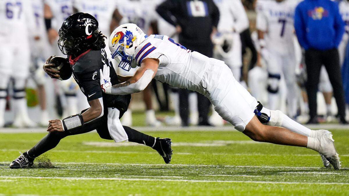 Cincinnati Bearcats quarterback Emory Jones (5) drives the ball as Kansas Jayhawks defensive lineman Austin Booker (9) tackles him to the ground during the NCAA college football game between the Cincinnati Bearcats and Kansas Jayhawks on Saturday, Nov. 25, 2023, at Nippert Stadium in Cincinnati. Kansas won 49-16.