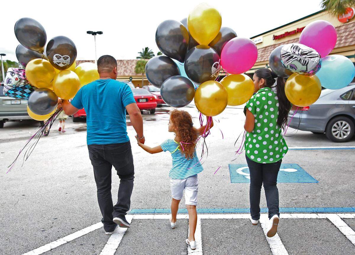 In this file photo from Dec. 31, 2013, Ashley Melgar celebrated her 7th birthday on New Years Eve with a handful of birthday and New Year balloons as she leaves the Party City store in South Miami with her father, Wilmer Melgar, left and sister Amada Wilmer, then-16, at right.