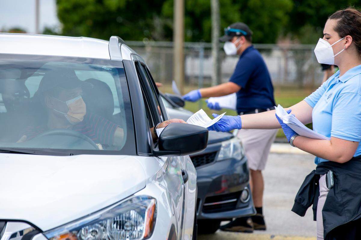 Recreational park leader Nicole Nieblas, 18, hands out a paper unemployment form to a Miami-Dade County resident after he waited in line at Slade park in Hialeah, Florida on Tuesday, April 7, 2020.