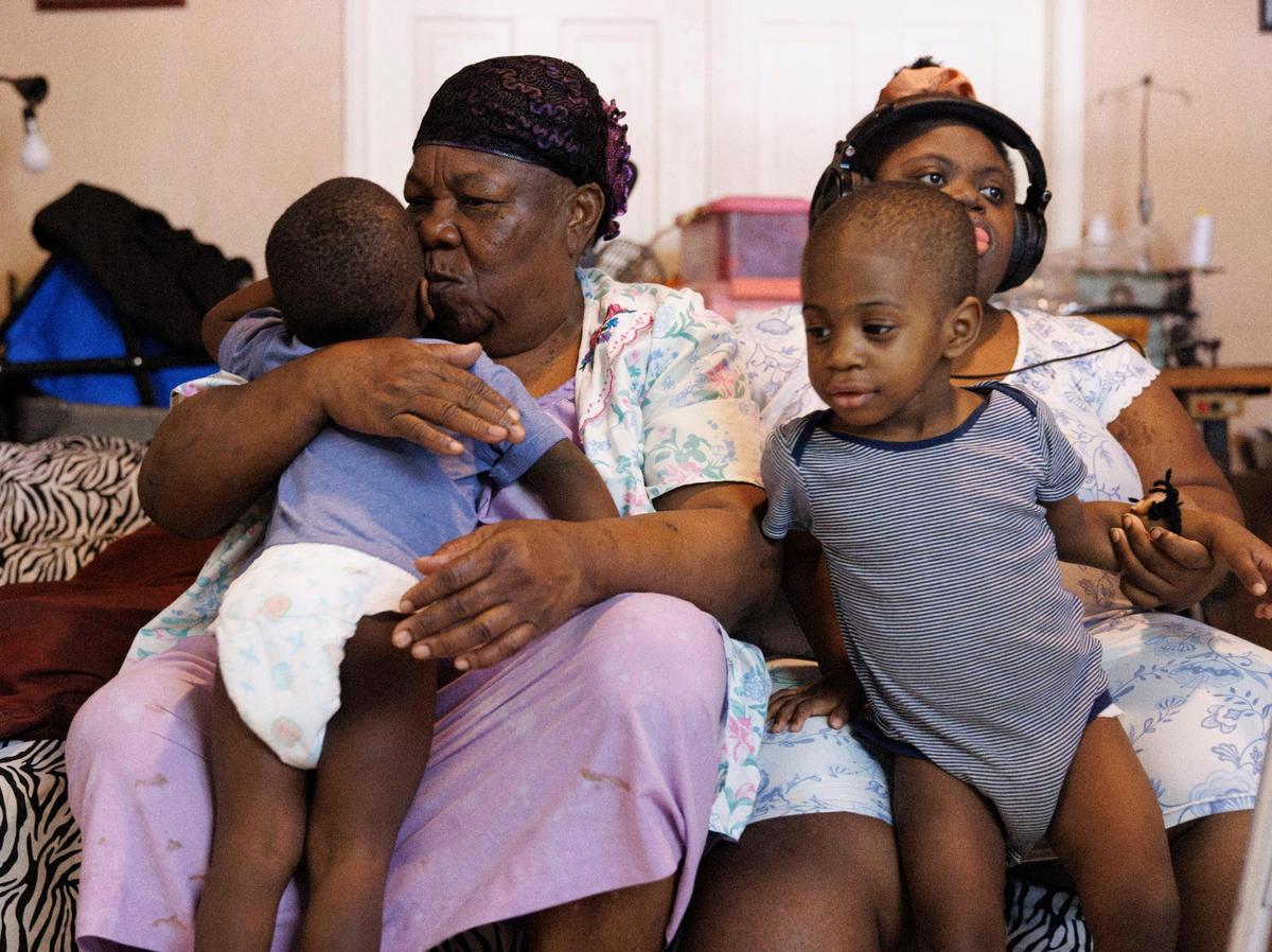 Mimose Martial, a 75 year-old grandmother who takes care of her toddler grandchildren and adult daughter with down syndrome, kisses Yeshousa, 2, while his twin, Samson, right, sits on the leg of Marie Martial, Mimose’s daughter, in their home. The rent went from $1,500 to $2,200 a few months ago, and Mimose has to rely on family for help. “They say it will go up again and I don’t know what I’m going to do,” said Mimose.