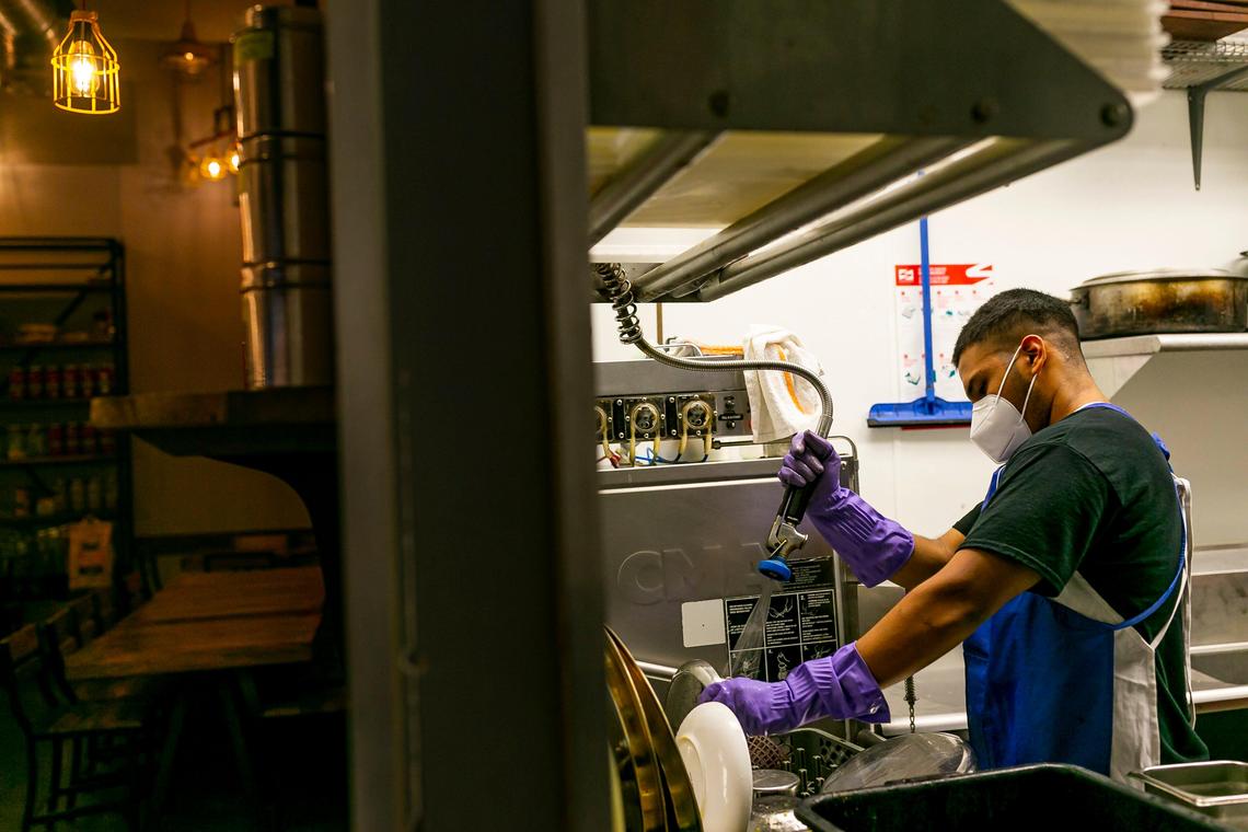 Roger Izaguirre, 21, a line cook at Ghee Indian Kitchen, washes dishes to help out at the restaurant. He is always aware that dishes coming back from tables could be contaminated with the coronavirus.
