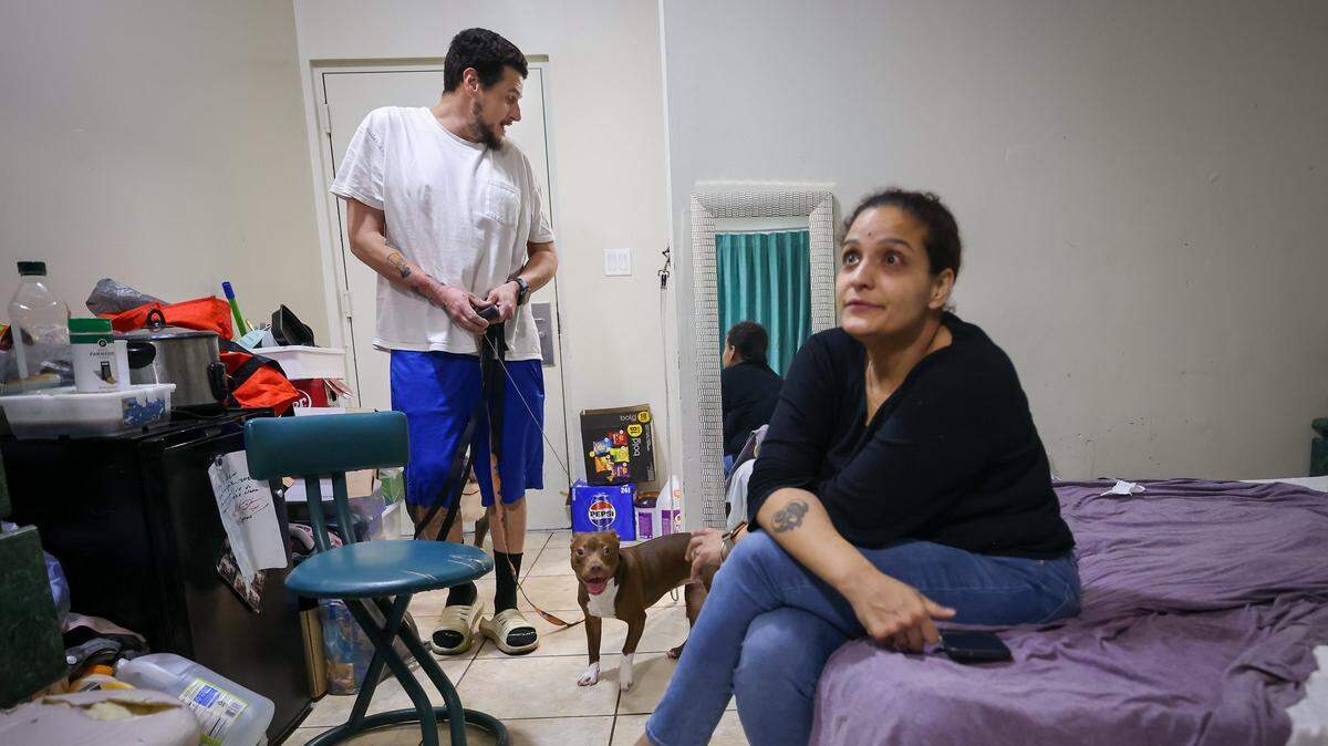 Michael Torres, left, prepares to take his dogs for a walk as Diana Olivo, right, reflects on the challenges of being unsheltered they and third children have been sharing a motel room for the last six months. She does not know how long they'll be able to afford to stay there on Wednesday, February 25, 2026, in Miami-Dade, Florida.