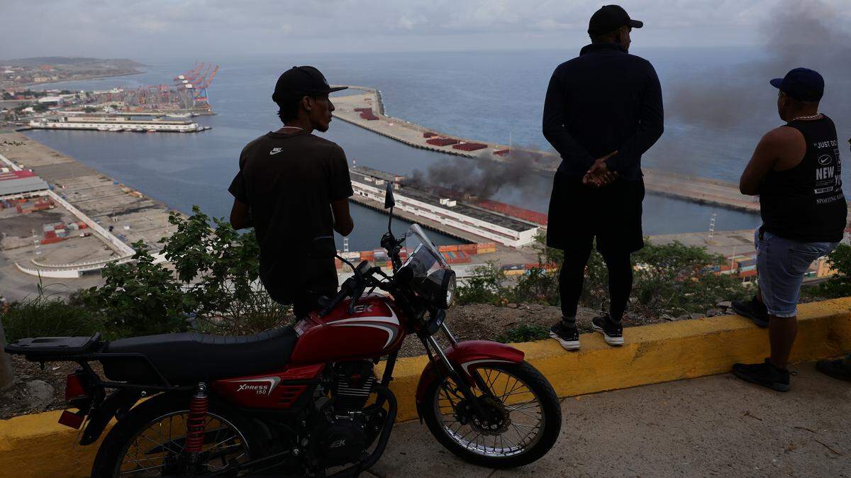 People watch smoke rise from the Port of La Guaira after explosions and low-flying aircraft are heard on Sunday in Caracas, Venezuela. A U.S. military operation captured Venezuelan President Nicolas Maduro and brought him to the United States to face criminal charges, drawing sharp criticism from Democrats and praise from Republicans.