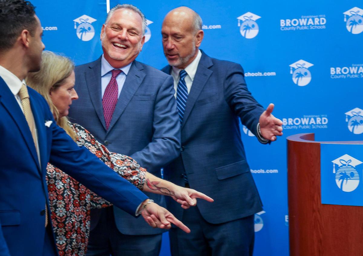 Superintendent Peter Licata, center, breaks into laughter as School Board members point to where he must stand for a group picture. Broward School Board held a special meeting to vote on the new superintendent’s contract at the Kathleen C. Wright Building in Fort Lauderdale, Florida on Tuesday, July 11, 2023. Left to right: School Board members Daniel Foganholi, Vice Chair Debra Hixon, Licata and Allen Zeman.