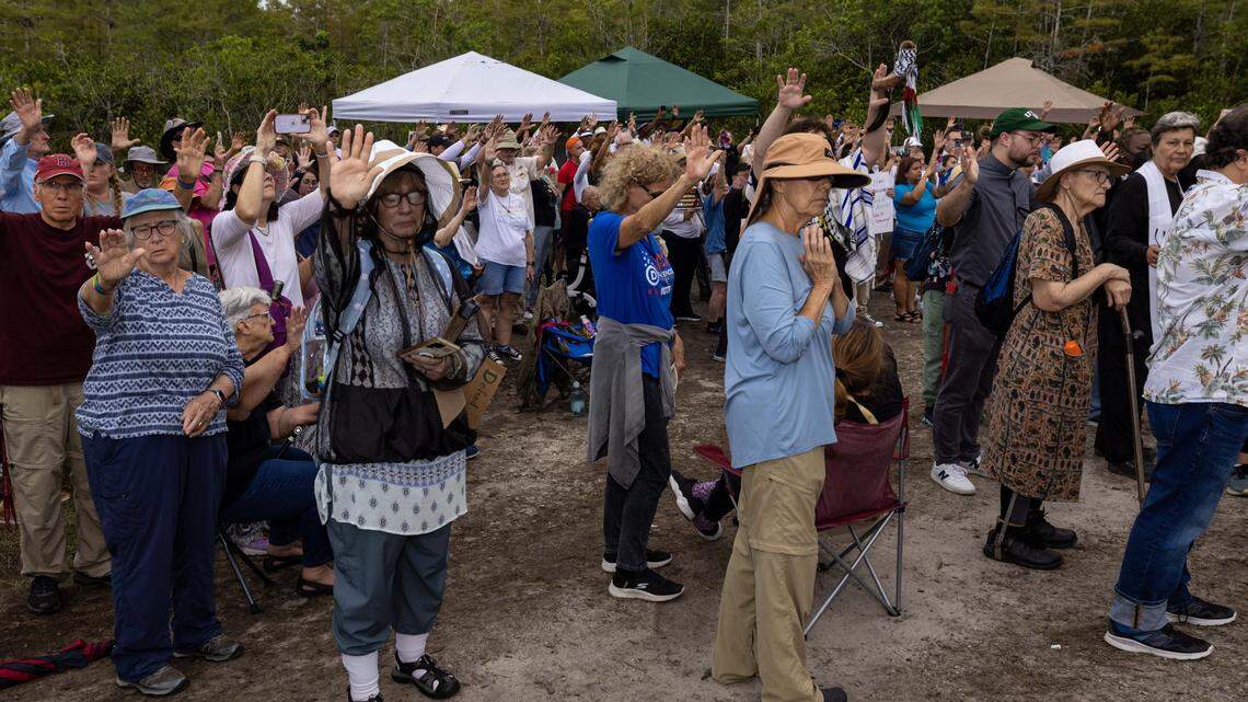 An group of interfaith leaders and followers hold their hands up in prayer outside Alligator Alcatraz. The spiritual event brings out people of all faiths each week to denounce the Florida immigrant detention center.
