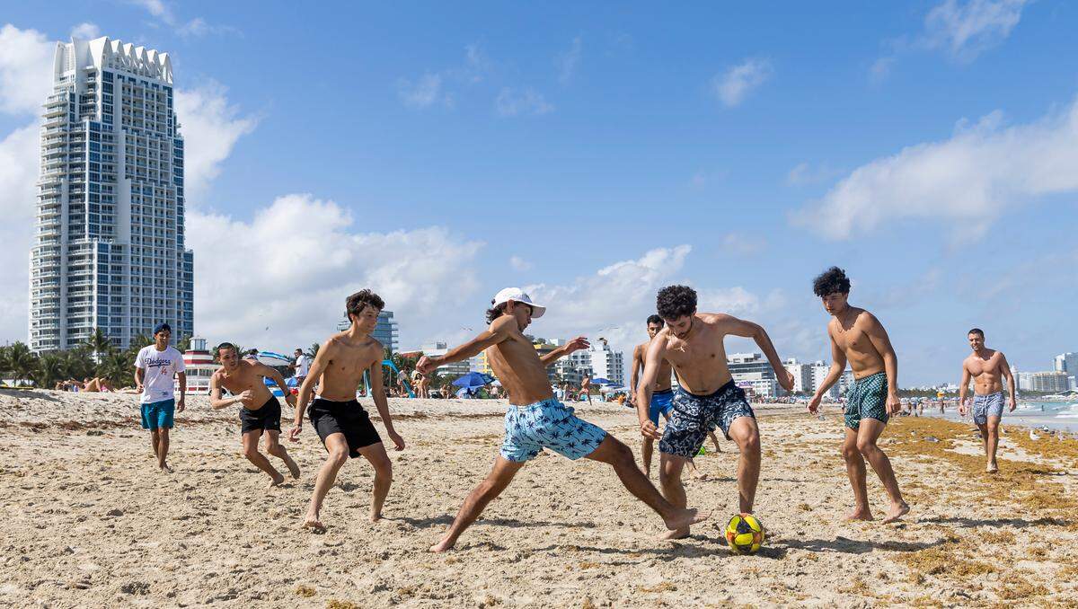 Juan Amato, center with ball, tries to make his way past Bryam Franco as they play soccer at South Pointe Beach on Friday, March 24, 2023 in Miami Beach, Fla. After two deadly shootings, city officials voted not to re-impose a midnight curfew, but implemented an emergency order banning alcohol sales after 6 p.m.