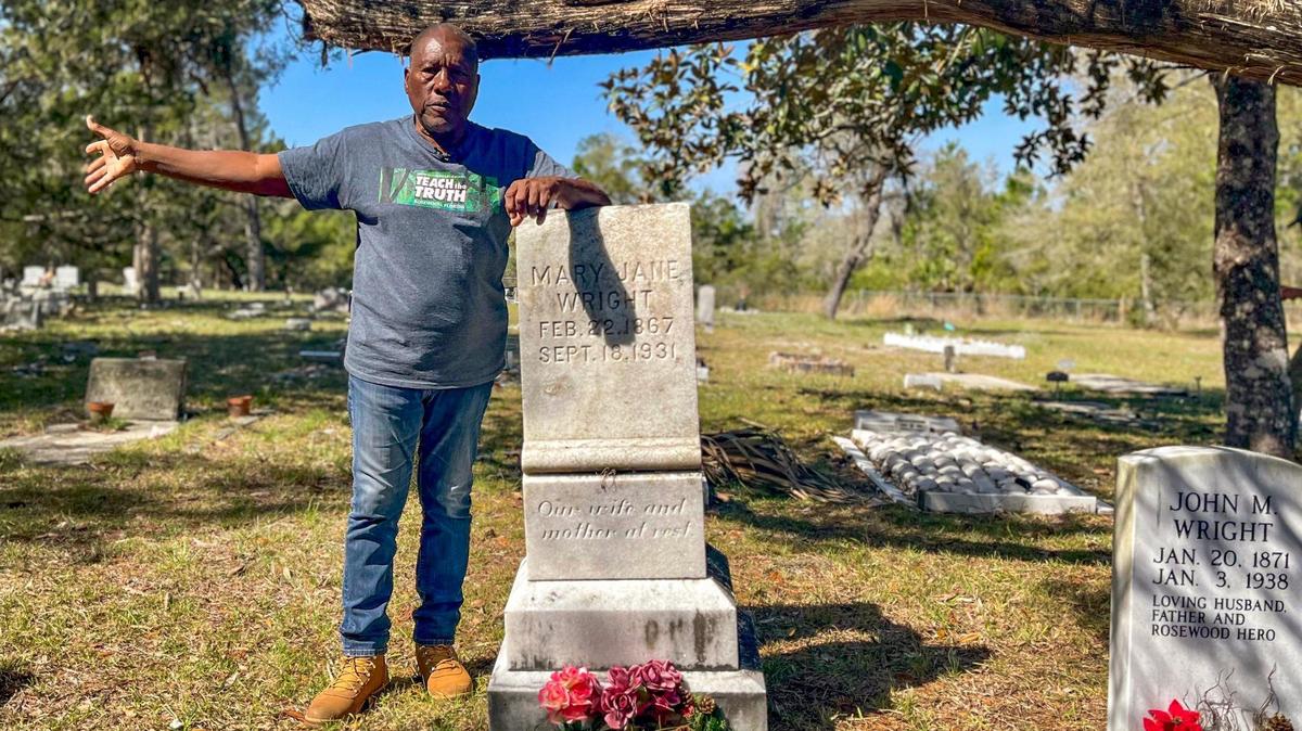 El historiador Marvin Dunn apoyándose en la lápida de Mary Jane Wright en el Cementerio Shiloh en Cedar Key, Florida, el 5 de marzo de 2023. Wright y su esposo John escondieron a mujeres y niños negros en el ático de su casa del norte de la Florida cuando comenzó el derramamiento de sangre de la masacre de Rosewood de 1923.